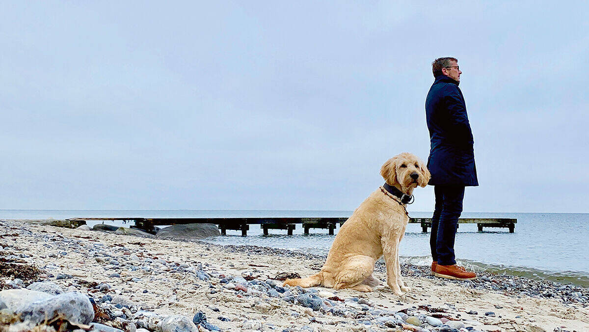 Mirko Kaminski mit Hund am Strand vor Steg. Auf diesem Bild ist alles inszeniert.